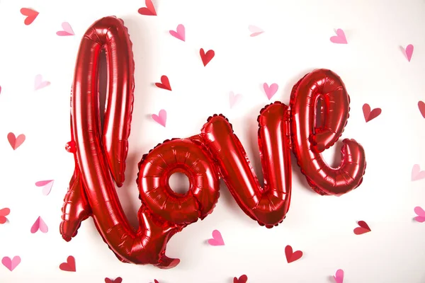 A balloon in the shape of the word love on white next to little valentines day hearts. — Stock fotografie