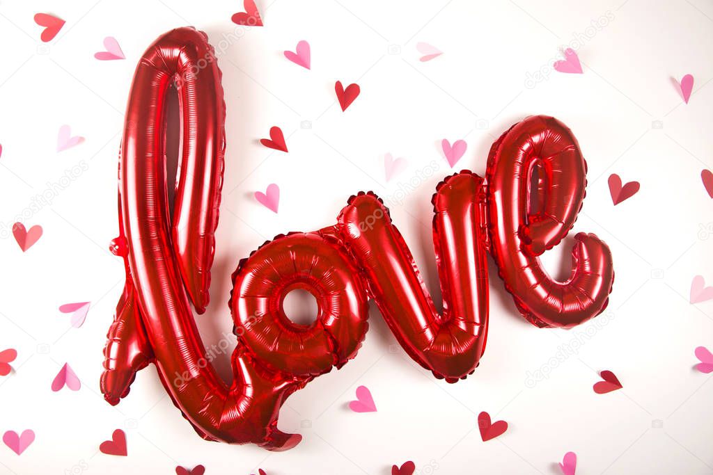 A balloon in the shape of the word love on white next to little valentines day hearts.