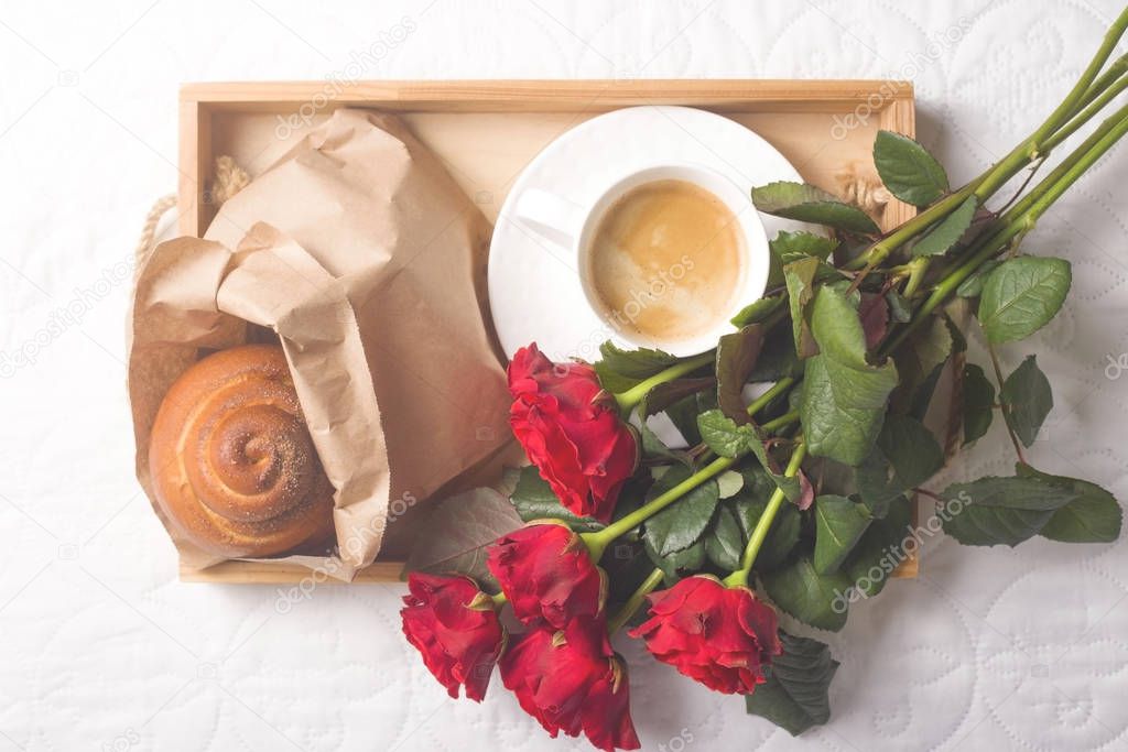 Coffee and muffins on a wooden tray. With a bouquet of flowers on the bed.