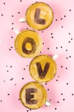 Aşk kelimesi pembe bir arka planda kahve köpüğüne yazılmış harflerden oluşur. Sevgililer Günü.