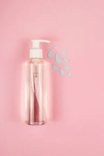 A clear bottle with a disinfector from which blue drops flowing with the word disinfect on pink. — Stock Photo, Image