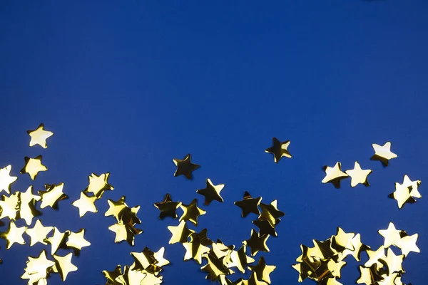 Złote konfetti zrobione z niebieskich gwiazd. Jasny wzór świąteczny — Zdjęcie stockowe