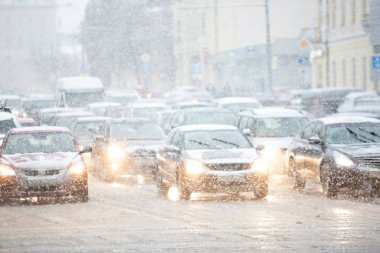 Farları açık arabalar kışın kar altında yol boyunca giderler. Trafik sıkışık. Yolda kar ve sulu kar.