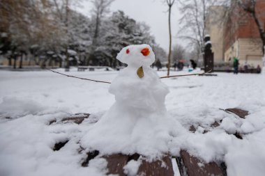 Şehir parkındaki bankta oturan komik bir kardan adam. Kırmızı gözlü kardan kadın. Yeni yıl tatili. kış eğlencesi