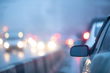 Arka plandaki dikiz aynası yağmurda yaklaşan arabaların bulanık farları.