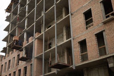 Yeni bir tuğla bina ve vinçle yükselen bir işçi.