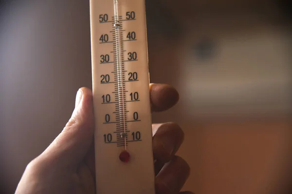 hand with a white plastic mercury thermometer shows the temperature in the room. measuring device