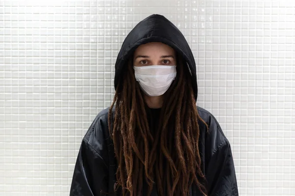 Ragazza in una maschera medica in un cappuccio contro un muro bianco — Foto Stock