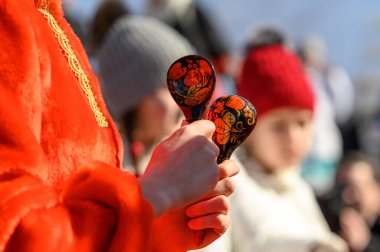 Geleneksel bir Rus aksesuarı olan tahta kaşıklar kırmızı folklor elbiseli bir kızın elinde. Karnaval festivali. Halk müziği enstrümanı. Tahta kaşıklarla oyna