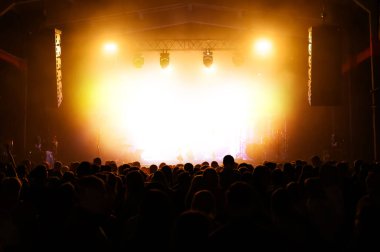 Bir konser festivalinde kalabalık sahnede bir sanatçıyı bekliyor. Müzik şovu afişi. Sahne ve insanların sırtı aydınlandı.