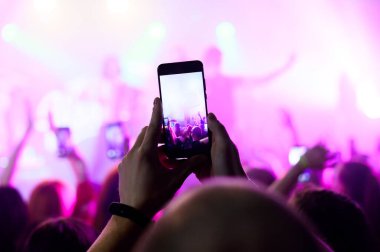 Kalabalıktaki bir konserde akıllı telefondan video çek. Müzik festivali. grup siluetleri parlak sahne ışıkları altında