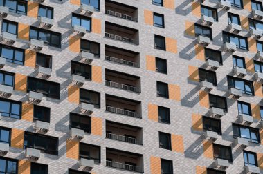 Gri-turuncu tuğlalı modern gökdelen, balkonlu ve pencereli. İpotekler için yeni binalar. Şehrin uyku alanları