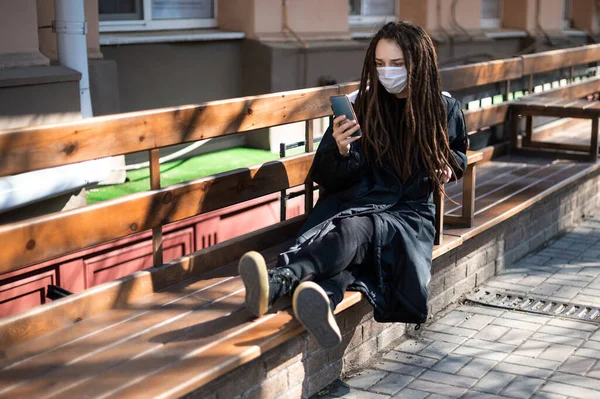 Girl Dreadlocks Protective Mask Her Face Sits Benches Smartphone Public — Stock Photo, Image