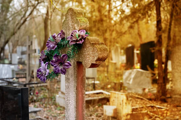 在墓地的坟墓上的一个古老花岗岩十字架上有紫色的人造花 Sepia墓地的照片 基督教葬礼 — 图库照片