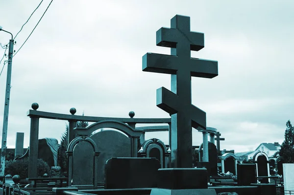 marble black cross on a grave in a cemetery. gloomy photograph of the evening cemetery. expensive marble tombstone