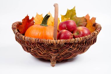 Beyaz bir arka plan üzerinde sepet dolu bir kabak ve elma ile bazı akçaağaç yaprakları