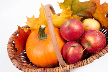 Beyaz bir arka plan üzerinde sepet dolu bir kabak ve elma ile bazı akçaağaç yaprakları