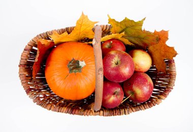 Beyaz bir arka plan üzerinde sepet dolu bir kabak ve elma ile bazı akçaağaç yaprakları