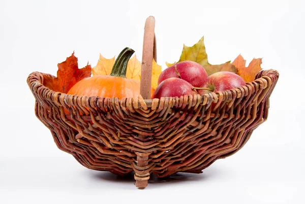 Beyaz bir arka plan üzerinde sepet dolu bir kabak ve elma ile bazı akçaağaç yaprakları