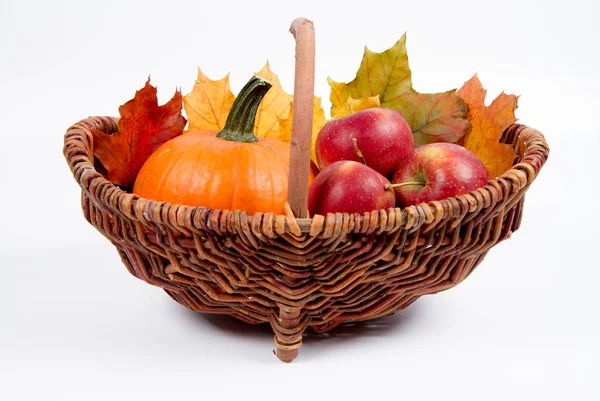 Beyaz bir arka plan üzerinde sepet dolu bir kabak ve elma ile bazı akçaağaç yaprakları