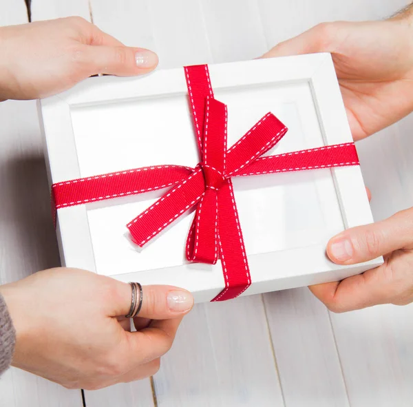 Man\'s and woman\'s hands exchanging a gift wrapped blank frame over a wooden background
