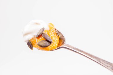 Beyaz bir arka plan üzerine bir kaşık krem ve kabak tohumları ile dekore edilmiş kabak ve havuç çorbası