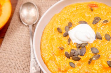 Kabak ve havuç çorbası bir ahşap zemin üzerine krema, maydanoz ve balkabağı tohumları ile dekore edilmiş