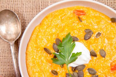 Kabak ve havuç çorbası bir ahşap zemin üzerine krema, maydanoz ve balkabağı tohumları ile dekore edilmiş