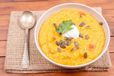 Kabak ve havuç çorbası bir ahşap zemin üzerine krema, maydanoz ve balkabağı tohumları ile dekore edilmiş