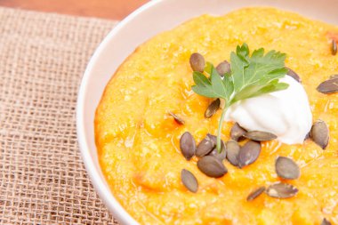 Kabak ve havuç çorbası bir ahşap zemin üzerine krema, maydanoz ve balkabağı tohumları ile dekore edilmiş