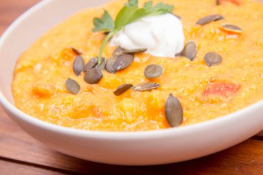 Kabak ve havuç çorbası bir ahşap zemin üzerine krema, maydanoz ve balkabağı tohumları ile dekore edilmiş