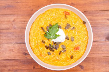 Kabak ve havuç çorbası bir ahşap zemin üzerine krema, maydanoz ve balkabağı tohumları ile dekore edilmiş