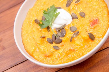 Kabak ve havuç çorbası bir ahşap zemin üzerine krema, maydanoz ve balkabağı tohumları ile dekore edilmiş