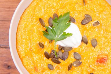 Kabak ve havuç çorbası bir ahşap zemin üzerine krema, maydanoz ve balkabağı tohumları ile dekore edilmiş