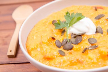 Kabak ve havuç çorbası bir ahşap zemin üzerine krema, maydanoz ve balkabağı tohumları ile dekore edilmiş