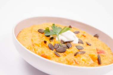 Kabak ve havuç çorbası Krem, maydanoz ve balkabağı tohumları üzerinde beyaz bir arka plan ile dekore edilmiş