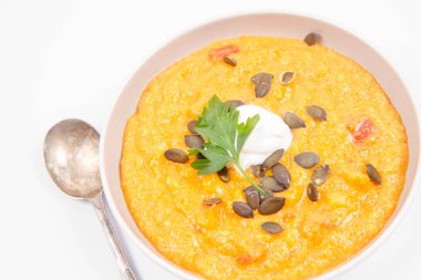 Kabak ve havuç çorbası Krem, maydanoz ve balkabağı tohumları üzerinde beyaz bir arka plan ile dekore edilmiş