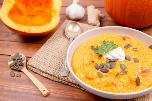 Pumpkin soup and pumpkins, pumpkin seeds, ginger and garlic on a wooden background