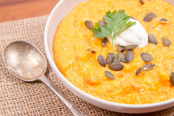 Kabak ve havuç çorbası bir ahşap zemin üzerine krema, maydanoz ve balkabağı tohumları ile dekore edilmiş