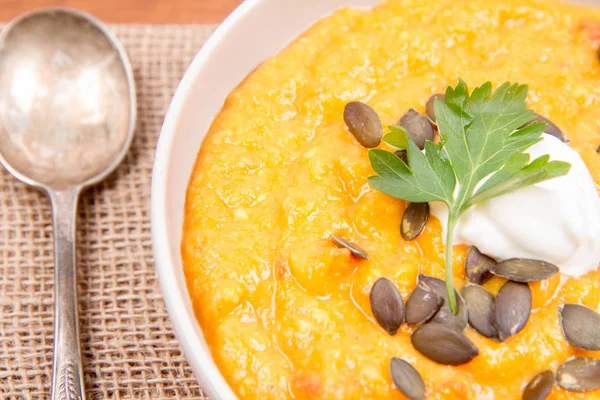 Kabak ve havuç çorbası bir ahşap zemin üzerine krema, maydanoz ve balkabağı tohumları ile dekore edilmiş