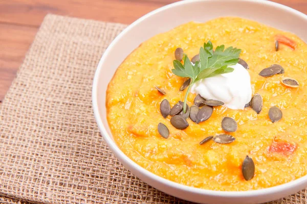 Kabak ve havuç çorbası bir ahşap zemin üzerine krema, maydanoz ve balkabağı tohumları ile dekore edilmiş