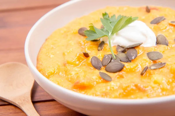 Kabak ve havuç çorbası bir ahşap zemin üzerine krema, maydanoz ve balkabağı tohumları ile dekore edilmiş