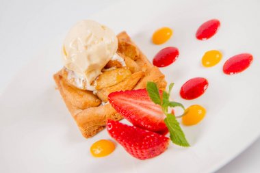 Bir çilek, meyve sosu ve bitki beyaz zemin üzerine elmalı pasta dondurma ile süslenmiş