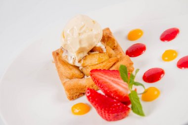 Bir çilek, meyve sosu ve bitki beyaz zemin üzerine elmalı pasta dondurma ile süslenmiş