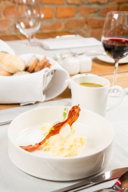 Bıldırcın yumurta, ekşi krema, patates püresi ve gevrek domuz pastırması ile kuzukulağı ve yeşil sebze çorbası Krem bir sürahi bir restoranda servis