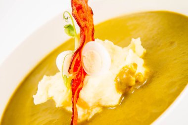 Bıldırcın yumurta, ekşi krema, patates püresi ve beyaz zemin üzerine gevrek domuz pastırması ile kuzukulağı ve yeşil sebze çorbası Krem