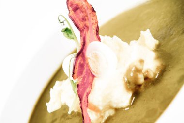 Bıldırcın yumurta, ekşi krema, patates püresi ve beyaz zemin üzerine gevrek domuz pastırması ile kuzukulağı ve yeşil sebze çorbası Krem