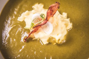 Bıldırcın yumurta, ekşi krema, patates püresi ve beyaz zemin üzerine gevrek domuz pastırması ile kuzukulağı ve yeşil sebze çorbası Krem