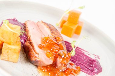 Beyaz bir backgorund üzerinde bir tabakta kavrulmuş patates, üvez ve bal sosu ördek göğsü, kırmızı lahana ile elma, kızartma