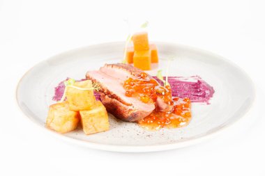 Beyaz bir backgorund üzerinde bir tabakta kavrulmuş patates, üvez ve bal sosu ördek göğsü, kırmızı lahana ile elma, kızartma